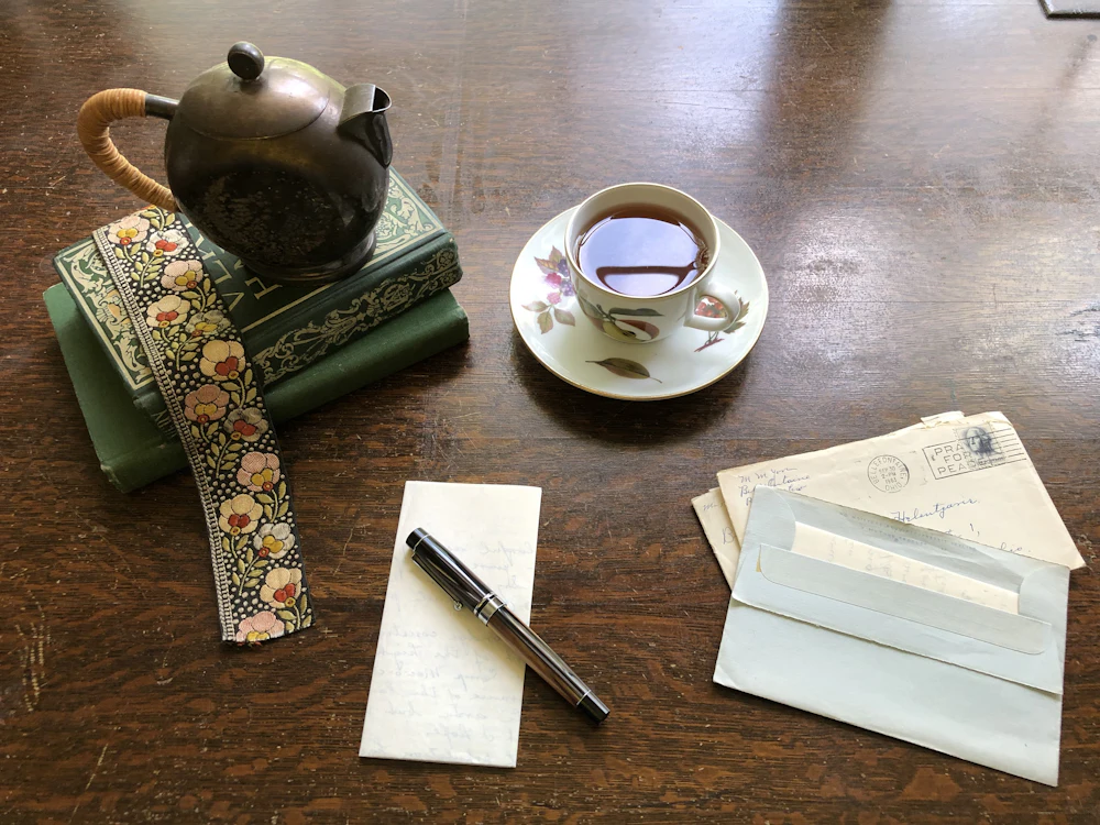 Una taza de té, una tetera, libros y cartas sobre una mesa de madera